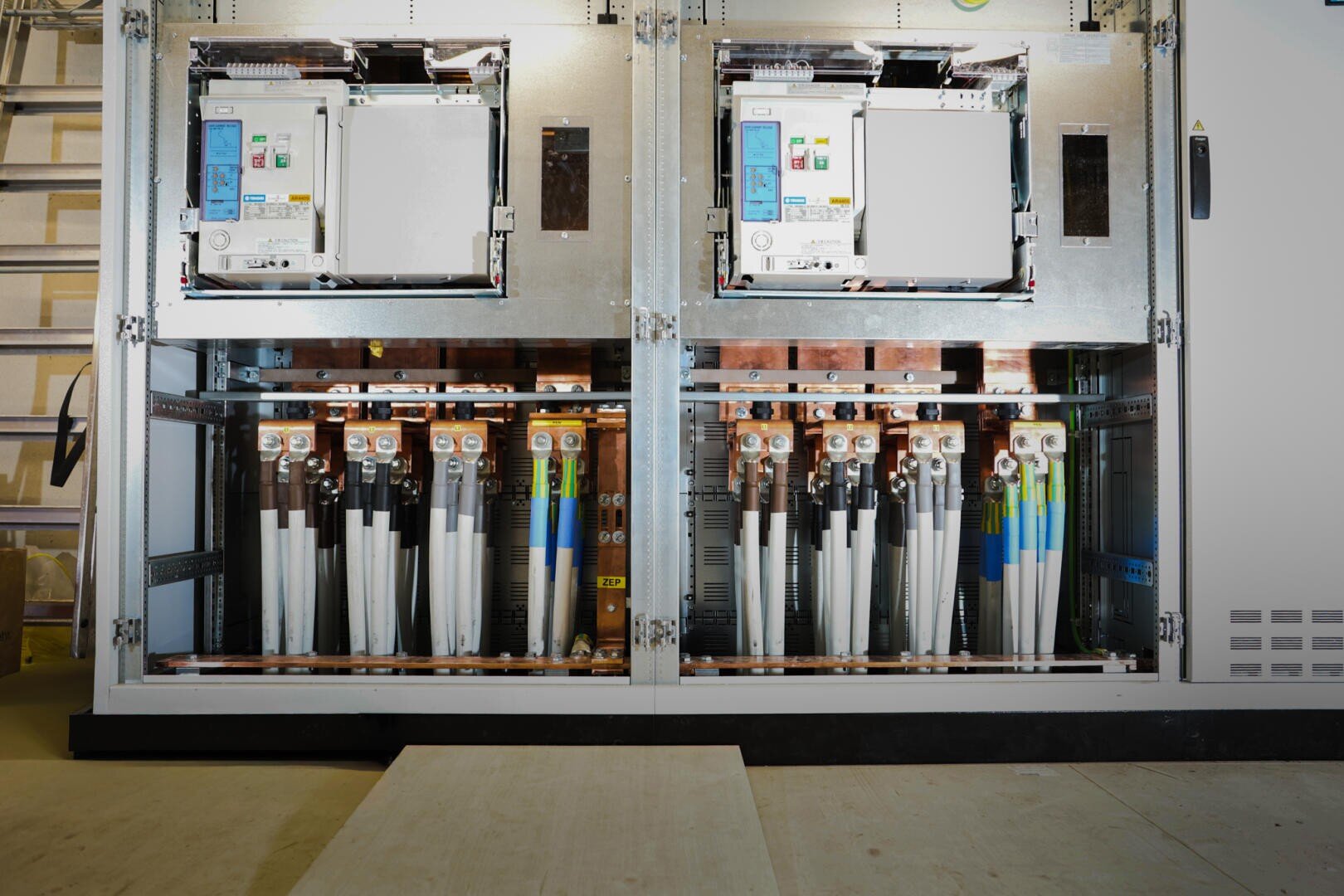 In einer geöffneten elektrischen Schalttafel sind Leistungsschalter, Kupferschienen, Drähte und Komponenten für die Stromverteilung und -steuerung übersichtlich angeordnet.