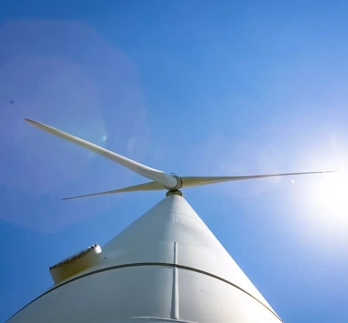 Blick auf eine weiße Windturbine vor einem strahlend blauen Himmel mit der Sonne im Hintergrund.