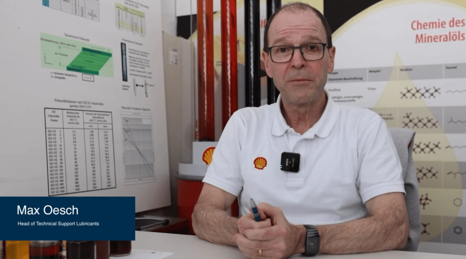 Ein Mann mit Brille und weißem Hemd mit Shell-Logo sitzt an einem Schreibtisch, hinter dem sich wissenschaftliche Tabellen und Schmierstoffproben befinden. Die Bildunterschrift lautet: Max Oesch, Head of Technical Support Lubricants.