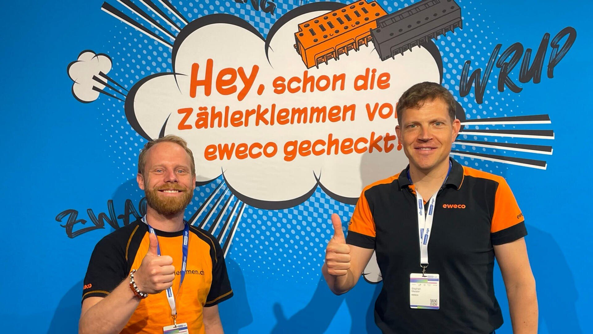 Zwei Männer in schwarzen und orangefarbenen T-Shirts mit eweco-Logos stehen vor einer blauen Wand im Comic-Stil, lächeln und zeigen den Daumen nach oben. Der Text im Hintergrund ist auf Deutsch verfasst und wirbt für eweco-Produkte.