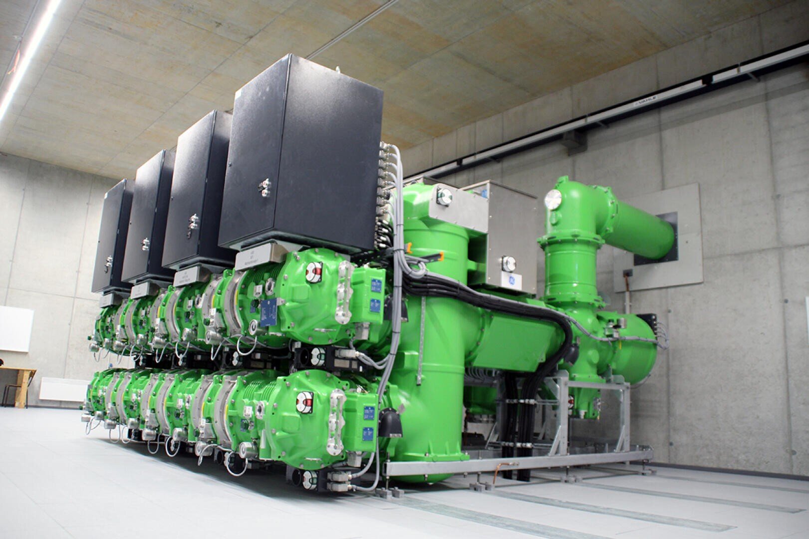 Große grüne elektrische Industrieanlagen mit schwarzen Schalttafeln, die in einem geräumigen, modernen Betonraum mit hoher Decke und offener Verkabelung installiert sind.