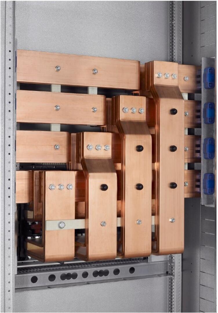 Nahaufnahme eines Metallgehäuses mit mehreren großen, flachen Kupferschienen, die vertikal und horizontal angeordnet und mit Bolzen verbunden sind. Die Stromschienen sind Teil einer elektrischen Verteilertafel. Auf der rechten Seite sind blaue Anschlüsse zu sehen.