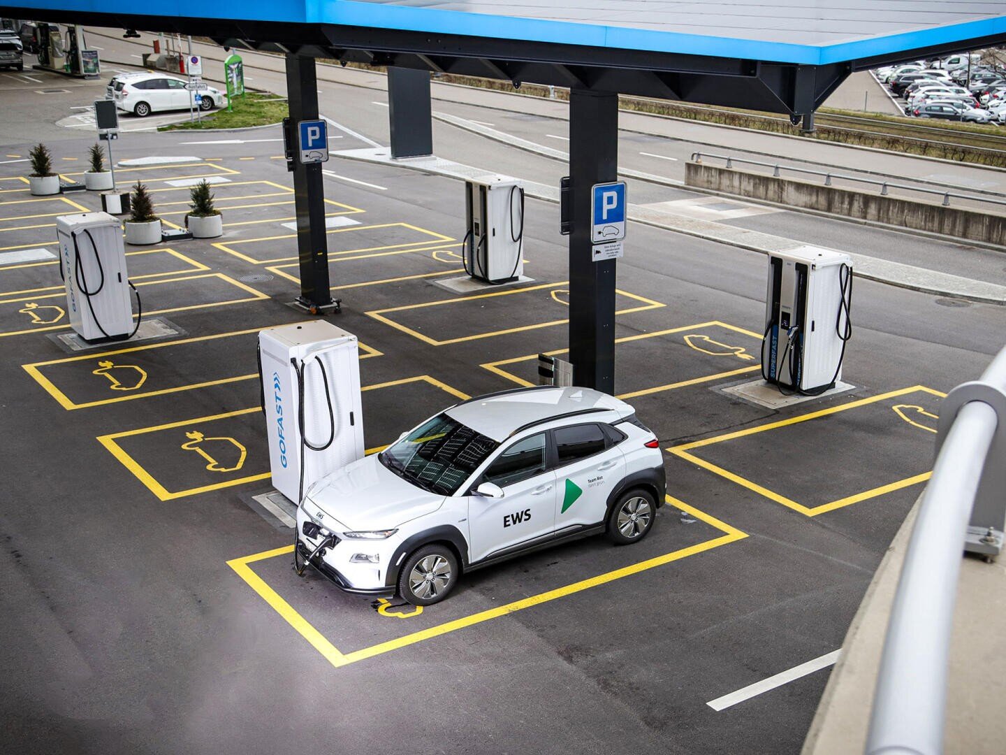Ein weißes Elektroauto, das auf einem modernen Parkplatz an einer Ladestation für Elektrofahrzeuge geparkt ist, umgeben von mehreren leeren Ladeplätzen und Ladegeräten.