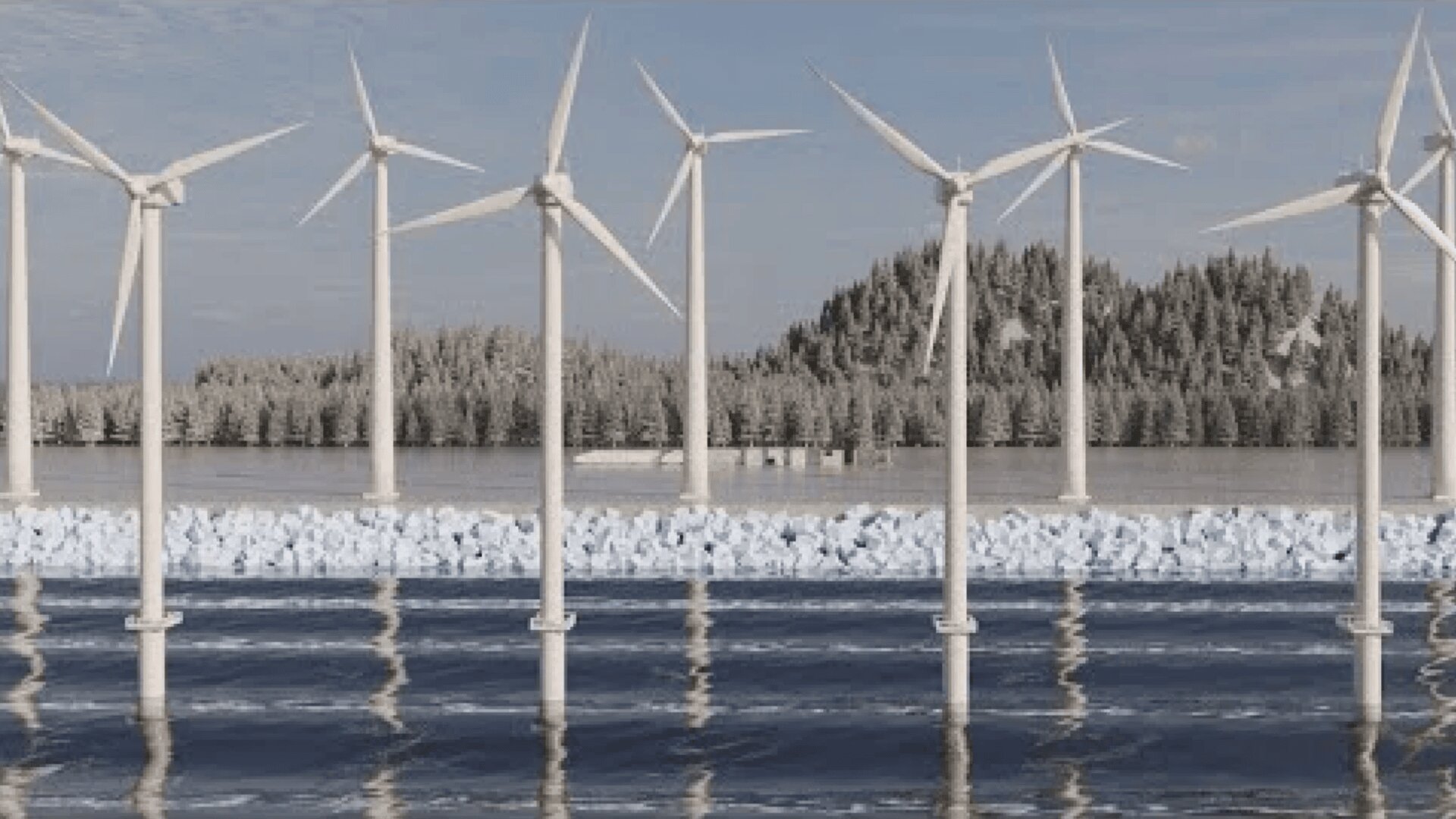 Rows of wind turbines stand in icy water, with snow-covered trees and a forested shoreline in the background under a cloudy sky.