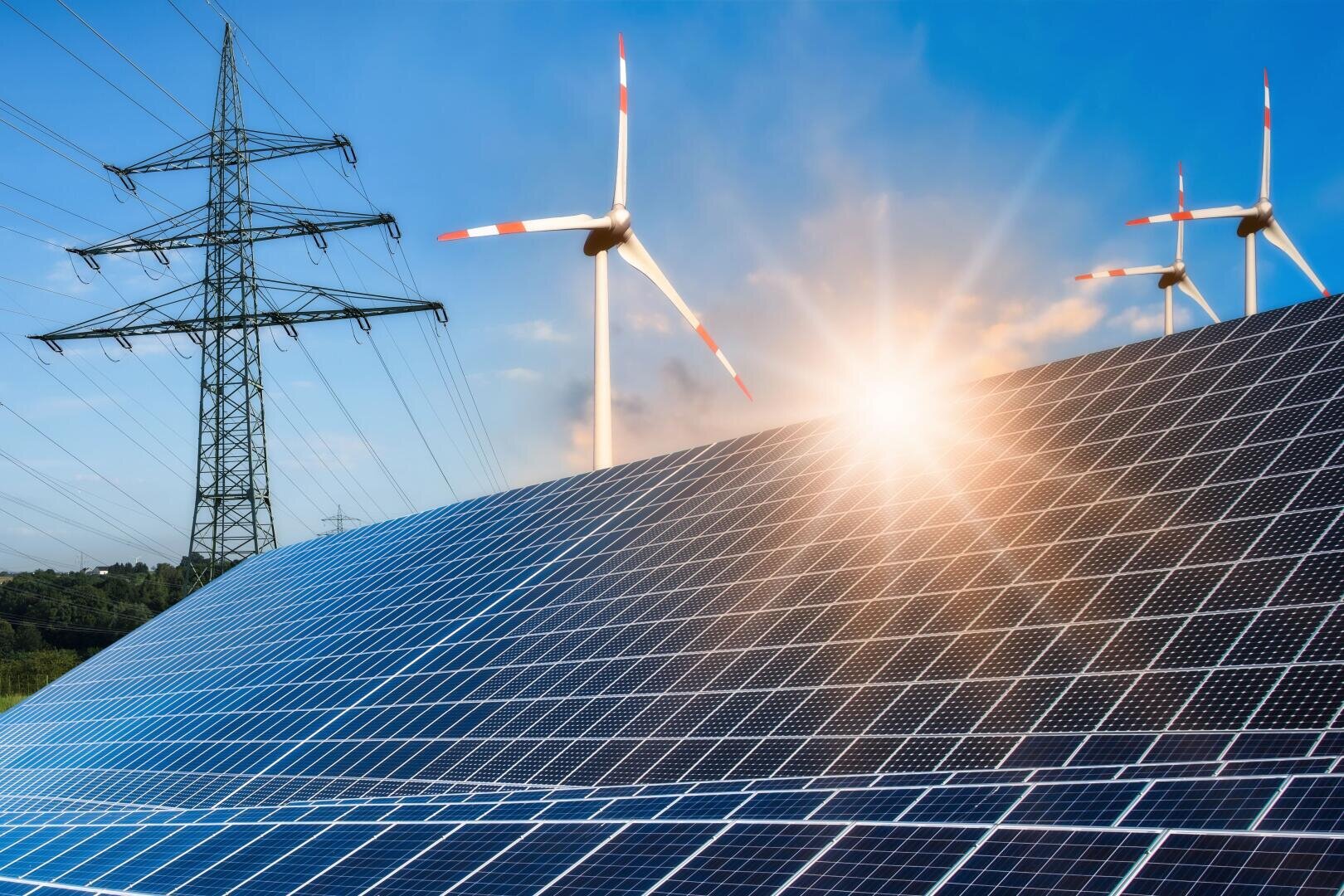 Im Vordergrund spiegeln Reihen von Solarmodulen das Sonnenlicht wider, im Hintergrund sind Windkraftanlagen und ein Strommast vor einem strahlend blauen Himmel zu sehen. Die Szene symbolisiert erneuerbare Energiequellen.