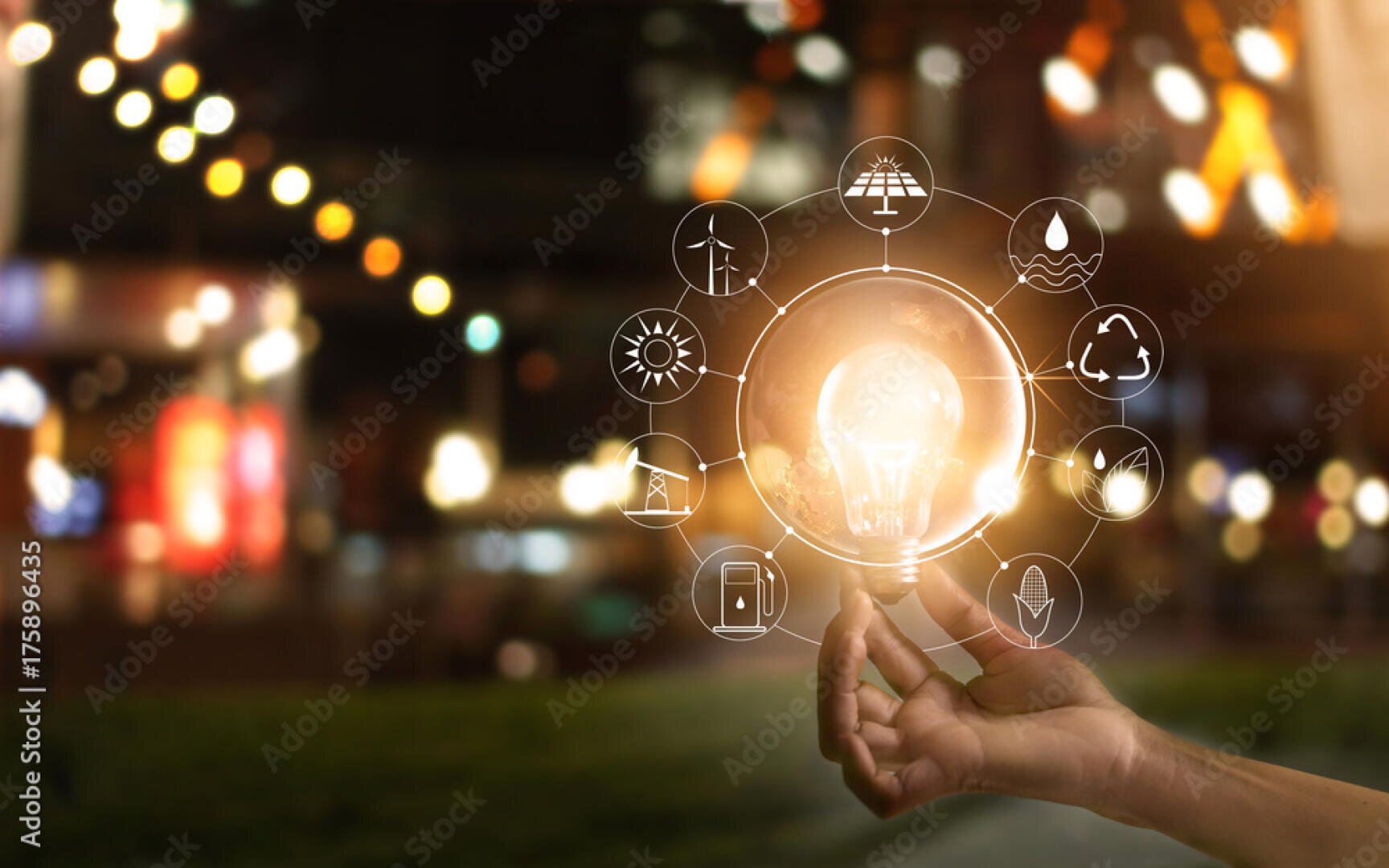 Eine Hand, die eine leuchtende Glühbirne mit beleuchteten Energie- und Nachhaltigkeitssymbolen um sich herum hält, vor einem unscharfen Hintergrund im Freien mit Bokeh-Lichtern.