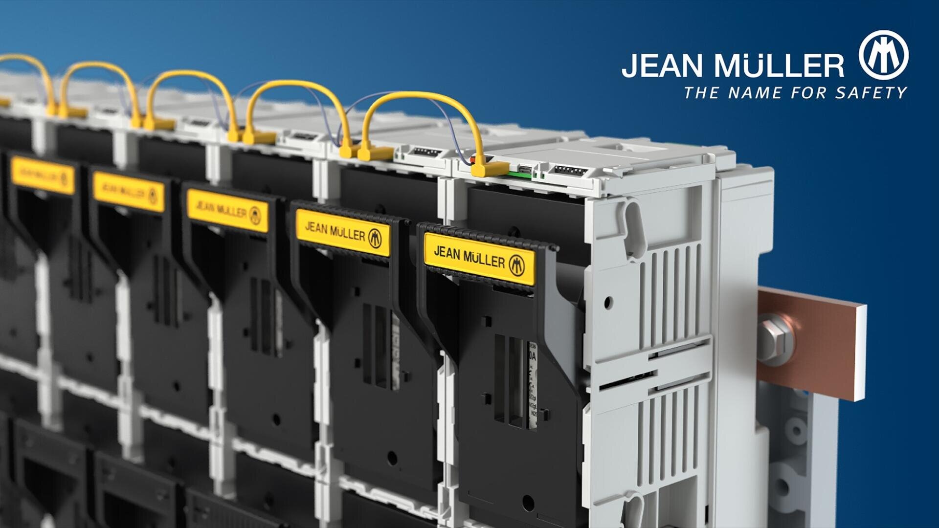 Nahaufnahme von elektrischen Bauteilen mit gelben Etiketten mit der Aufschrift JEAN MÜLLER, die durch gelbe Drähte verbunden sind, vor einem blauen Hintergrund mit dem Logo JEAN MÜLLER - THE NAME FOR SAFETY in der oberen rechten Ecke.