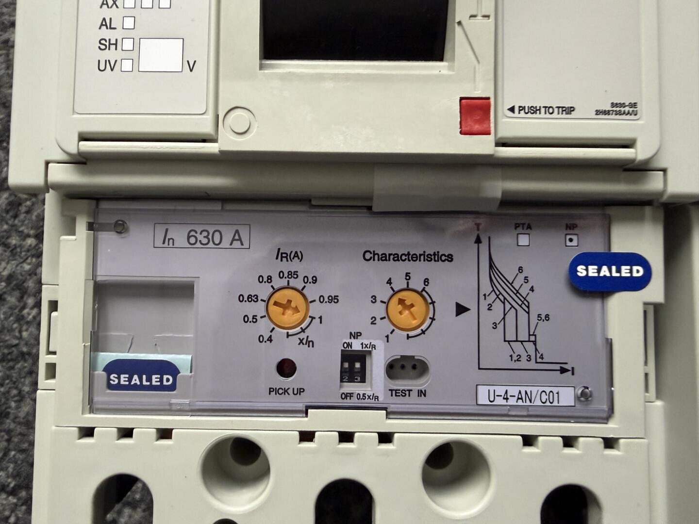 Nahaufnahme einer elektrischen Schalttafel mit der Aufschrift 630 A. Verschiedene Einstellräder, Knöpfe, Tabellen und Schalter sind sichtbar, zusammen mit blauen SEALED-Aufklebern und technischen Markierungen für Einstellungen und Eigenschaften.