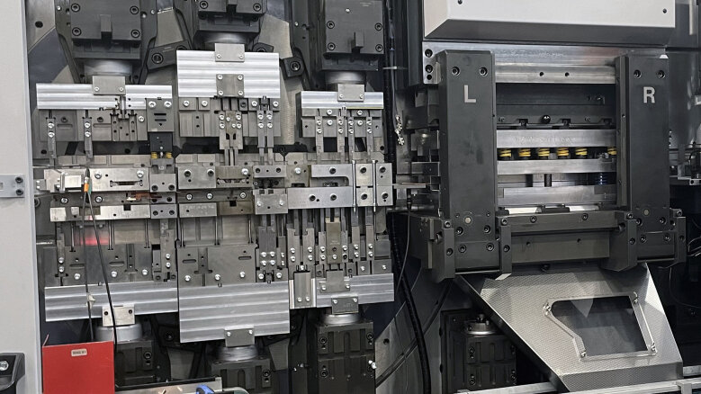 Nahaufnahme einer komplexen Industriemaschine mit verschiedenen Metallteilen, Bolzen und Federn. Die Maschine verfügt über beschriftete Abschnitte L und R und scheint für Präzisionsfertigung oder Montage verwendet zu werden.